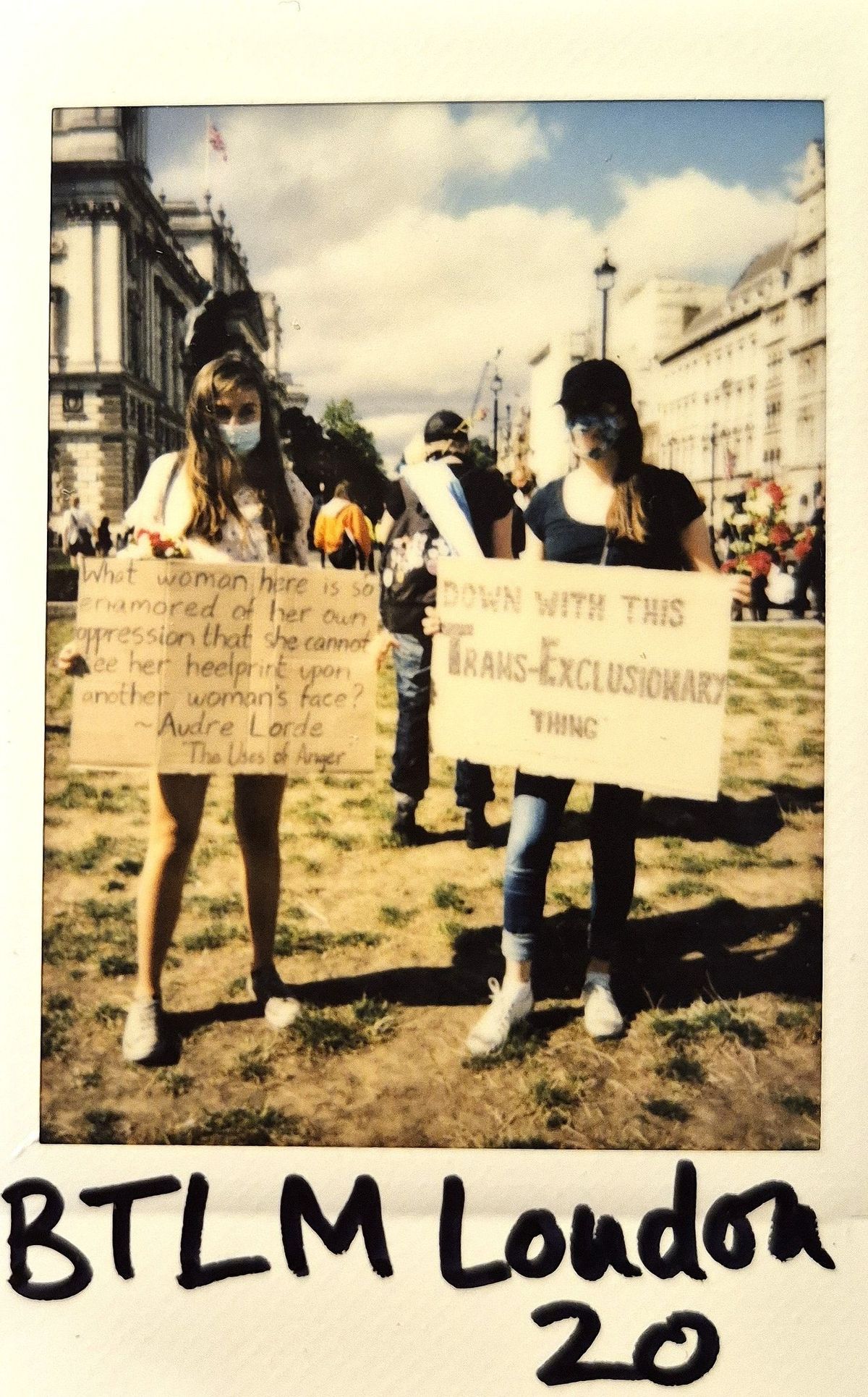 Two masked individuals hold signs at a protest in London.