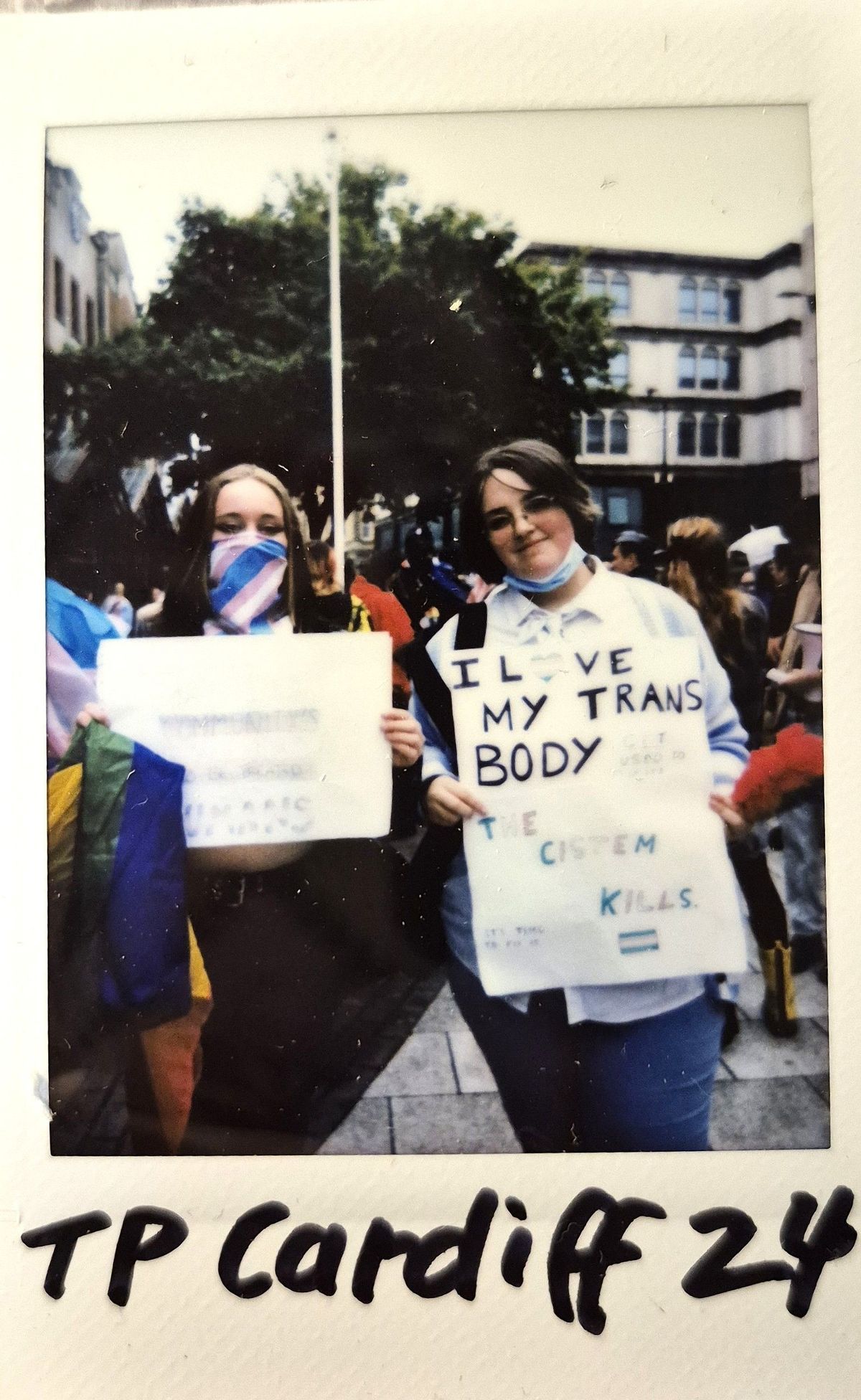 Two people at a protest hold signs advocating for transgender rights in a public gathering area.