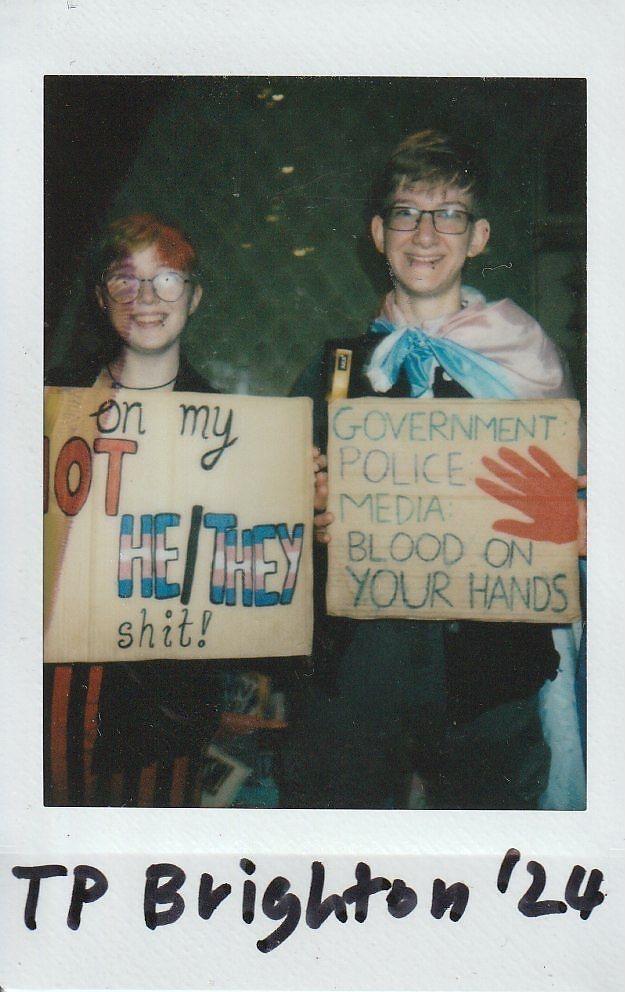 Two people are holding placards and grinning at the camera.