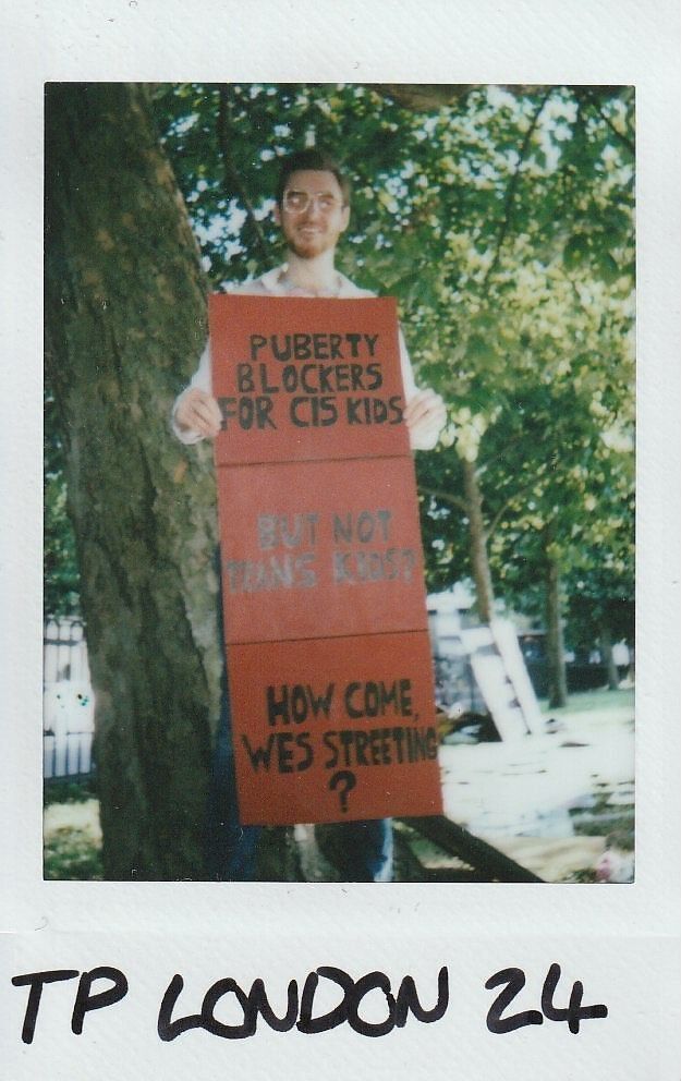 A person stands by a tree holding a sign which says "Puberty blockers for cis kids but not trans kids. How come Wes Streeting?"