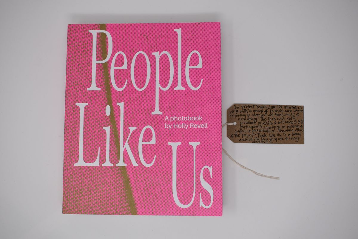 The image features a photobook titled "People Like Us" by Holly Revell, which has a pink cover with a green line through it. Next to it is a brown tag with writing on it.