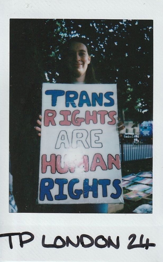 A person holds a sign reading "Trans Rights Are Human Rights" during an outdoor event.