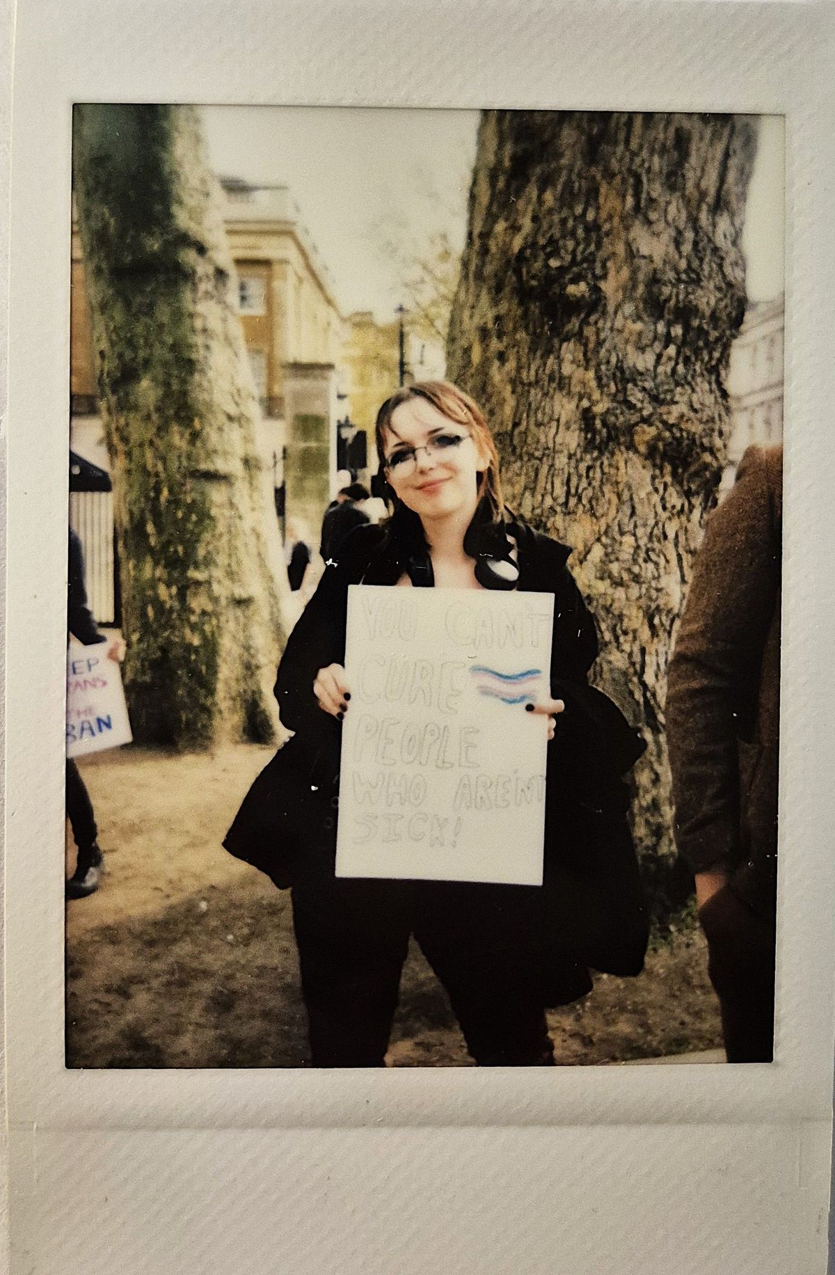 A person stands outdoors holding a sign that reads, "You can't cure people who aren't sick!"