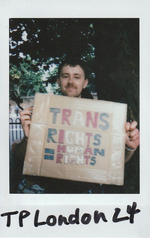 A person is holding a cardboard sign that reads "Trans rights are human rights" outdoors.