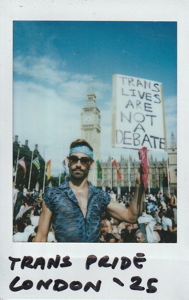 A person holds a sign saying "Trans Lives Are Not a Debate" stood in front of a crowd with Big Ben in the background.