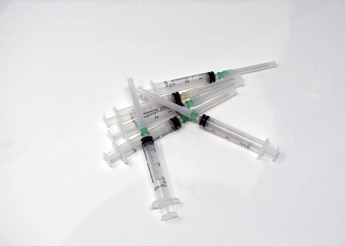 A pile of several unused syringes is scattered randomly on the plain white surface.