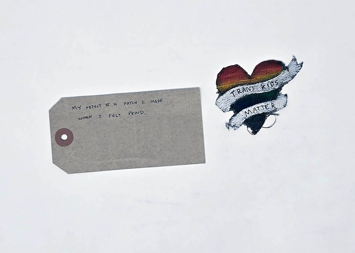 Badge patch & tag ; cotton fabric heart shaped hand painted with rainbow colours and white banner slogan " Trans Kids matter".