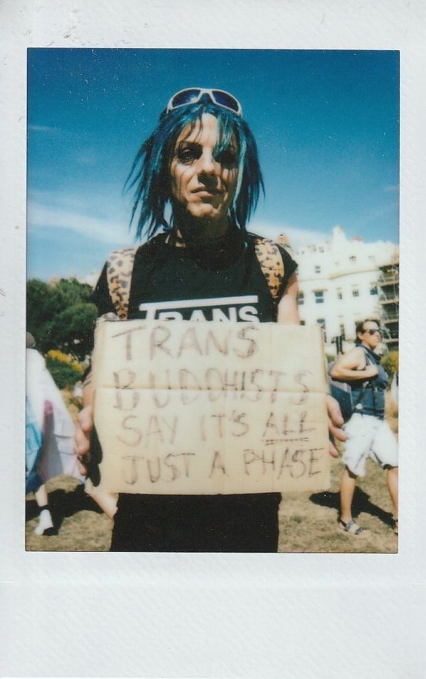 A person with blue hair holds a sign that says, "Trans Buddhists say it's all just a phase".