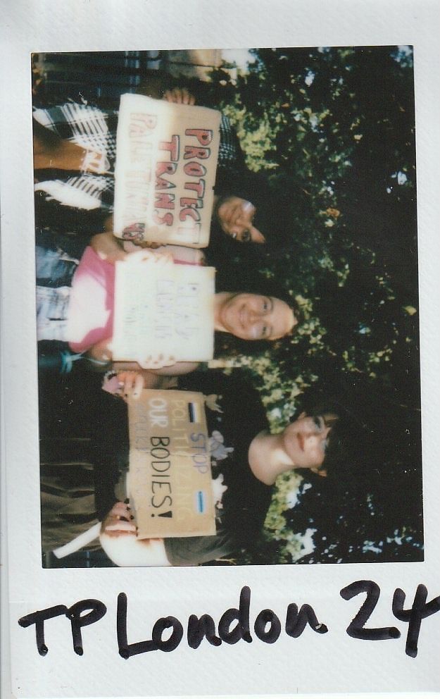 Three individuals are holding signs advocating for trans rights at an outdoor gathering in London.