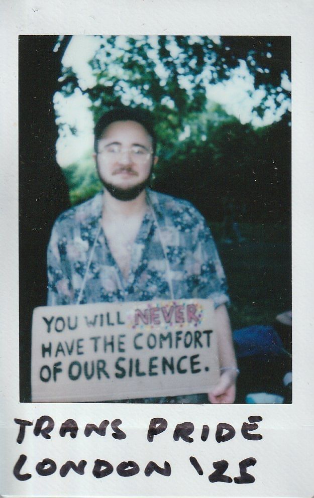 A person holds a sign reading, "You will never have the comfort of our silence".