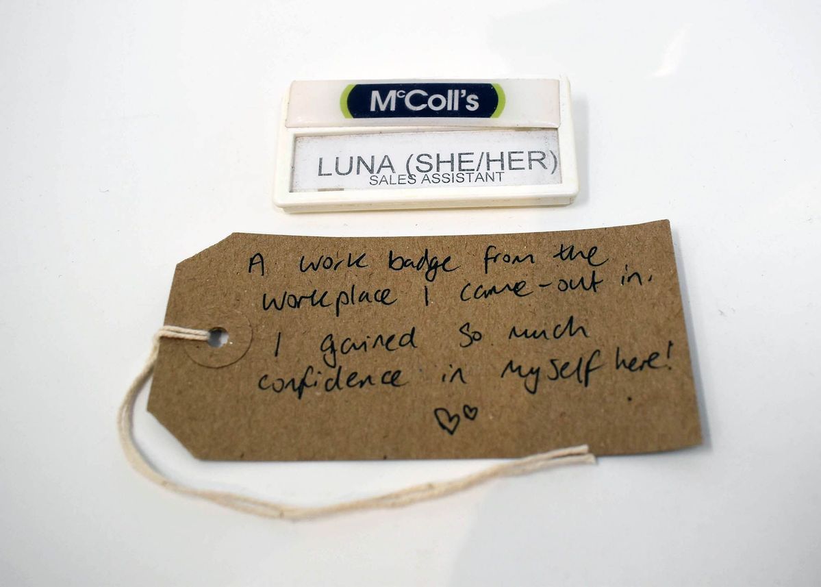 A McColl's employee name badge stating "LUNA (SHE/HER) SALES ASSISTANT" with a handwritten luggage tag.