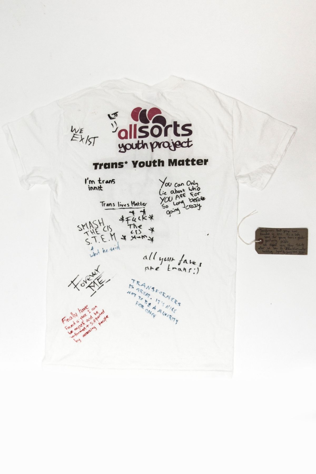 Back of the white T-shirt with the logo "allsorts youth project" at the top. Various signatures and handwritten slogans written across the back in blue, black, and red inks.