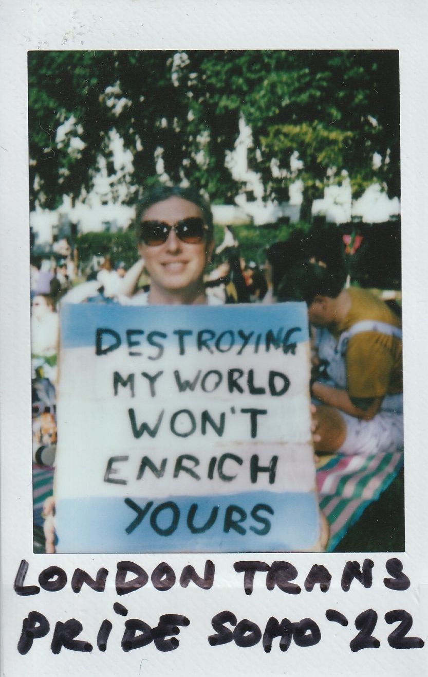 A person at London Trans Pride in Soho '22 holds a sign reading: "Destroying my world won't enrich yours".