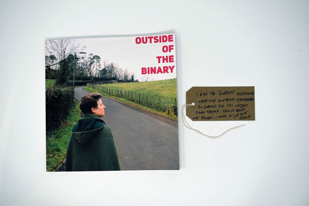 Outside of the Binary book. Cover photo is a person in a green cloak walking along a rural road. Also, a brown luggage tag.