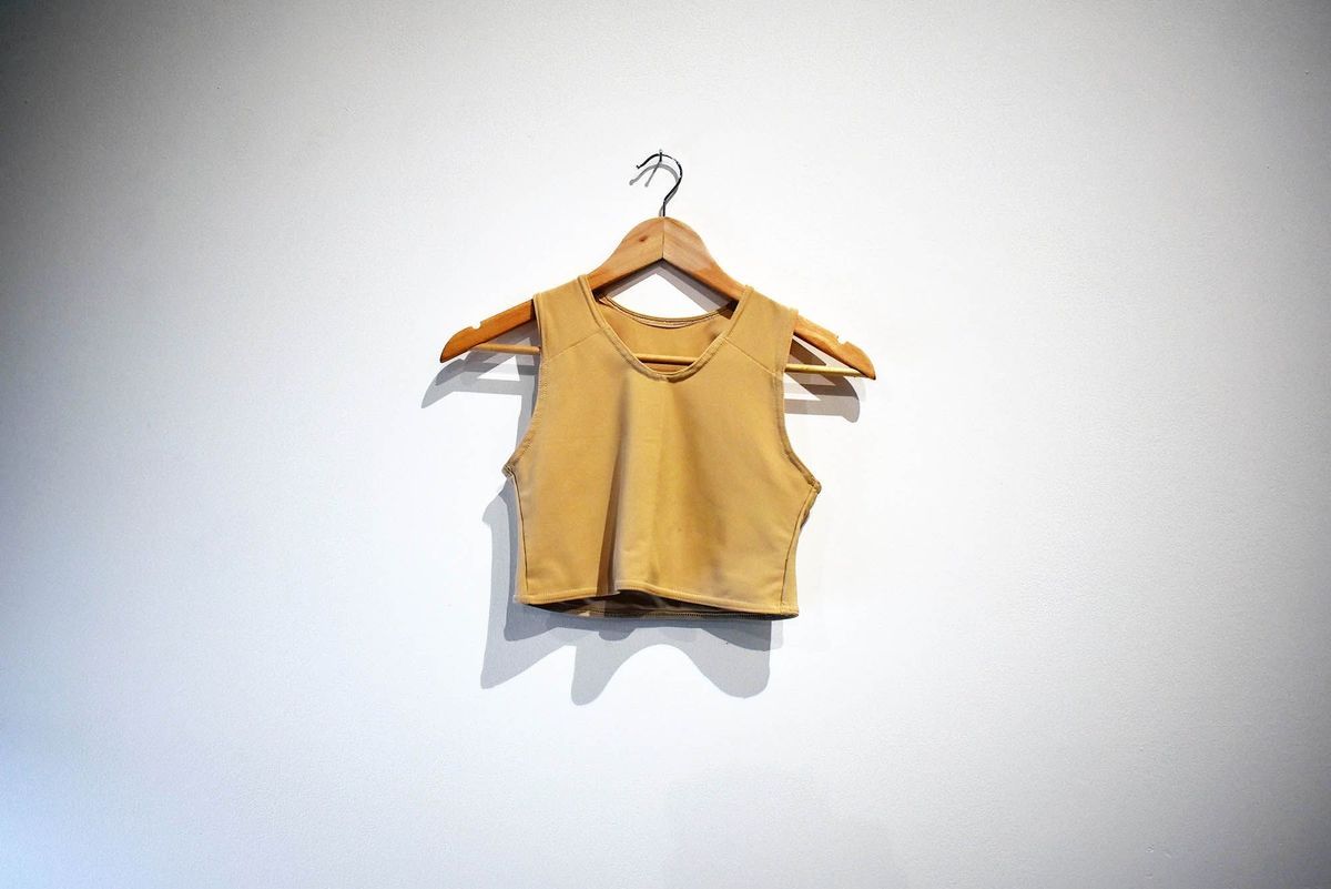 A beige cropped tank top is hanging on a wooden hanger against a plain white wall.