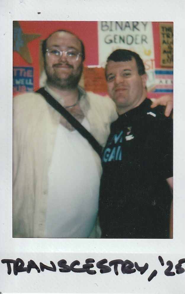 Two people smiling stand together in front of colorful posters.