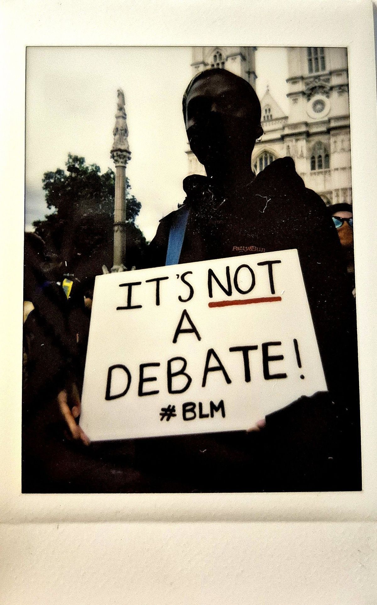 A person holds a sign reading "IT'S NOT A DEBATE! #BLM" at a protest.