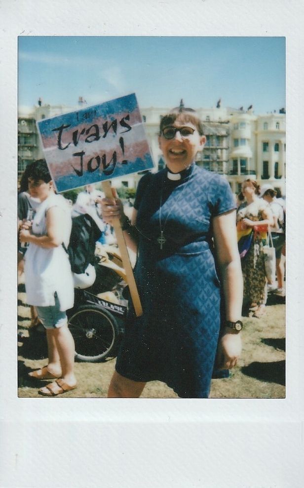 A person is smiling, holding a "Trans Joy!" sign.