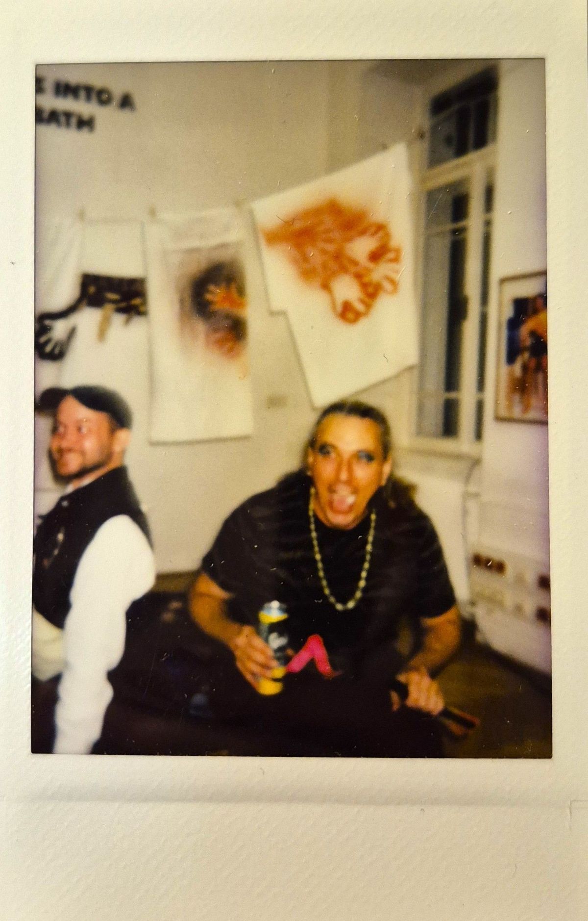 Two people are in a room with colorful art and a beverage.