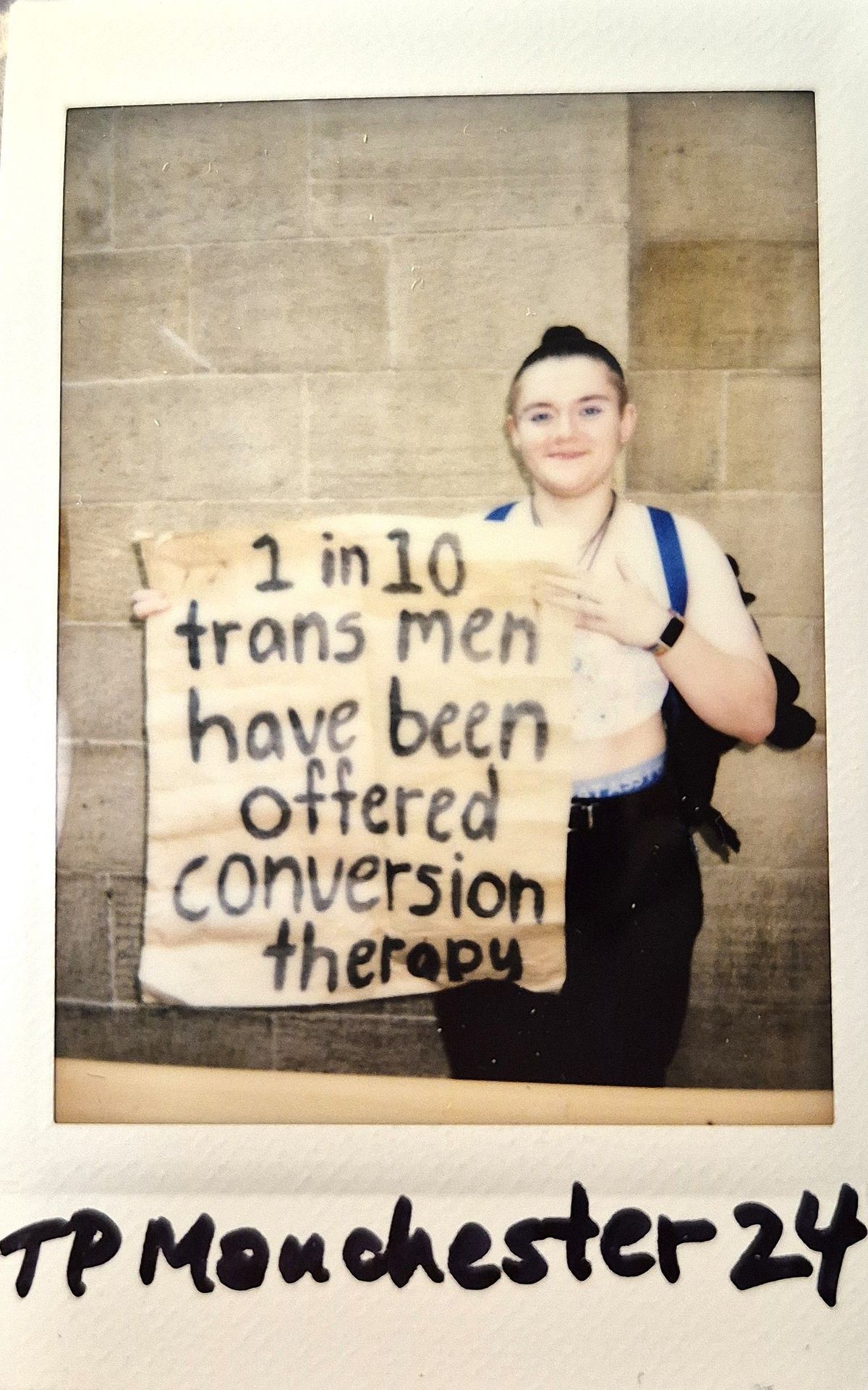 A person is holding a sign reading, "1 in 10 trans men have been offered conversion therapy".