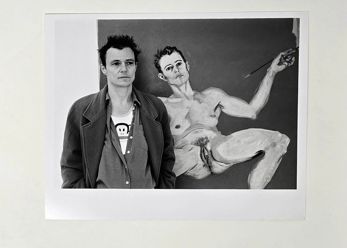 A black and white photograph of a person stood in front of a painting.