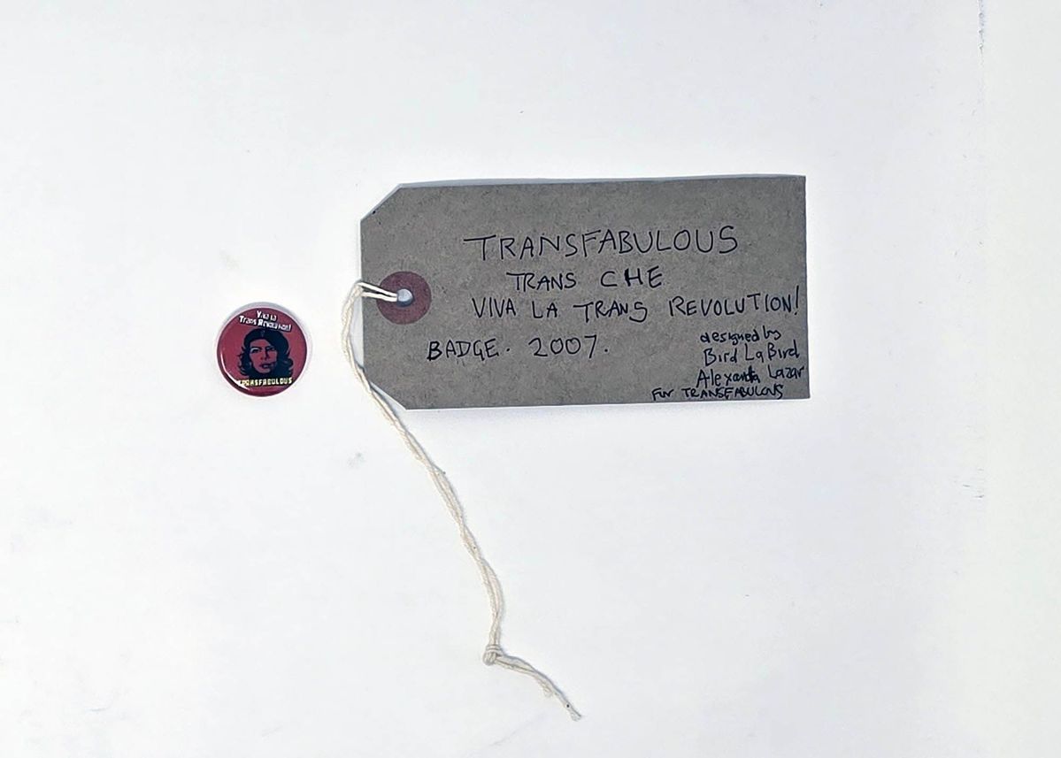 Pink badge with Che Guevara style picture of head wearing beret with blue eye shadow & slogan "Viva la Trans Revolution! Transfabulous