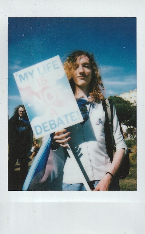 A person stands outdoors holding a sign reading "My life is not a debate".