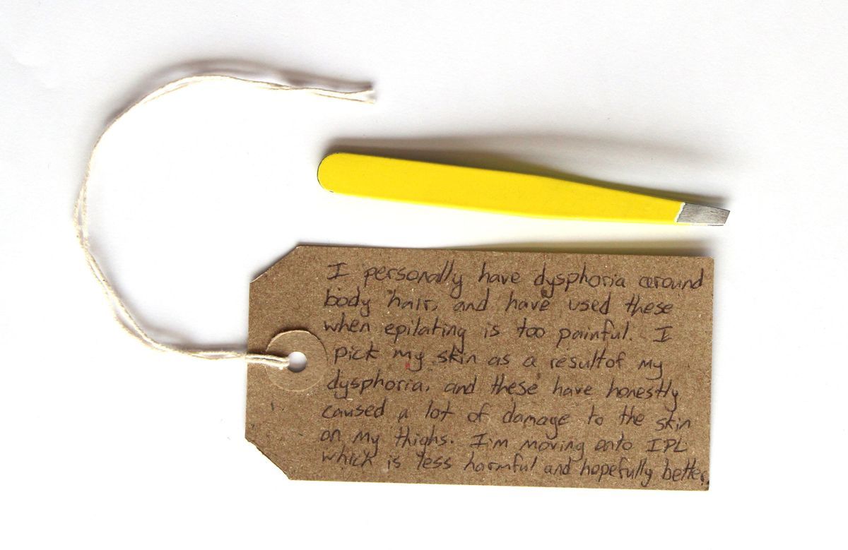 The image shows a cardboard tag with handwritten text and a pair of yellow tweezers on white background.