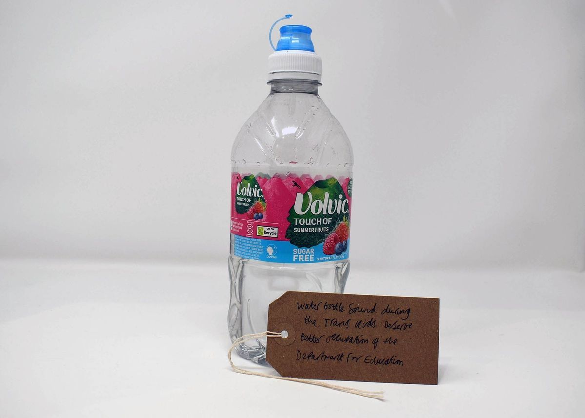 An empty plastic Volvic Touch of summer fruits water bottle. With a brown, handwritten luggage tag.