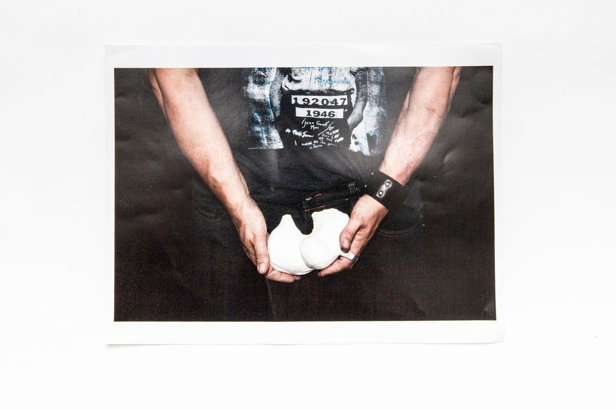 Photo shows lower body of figure in black T shirt & leather wristband holding plaster cast at hip/groin height.