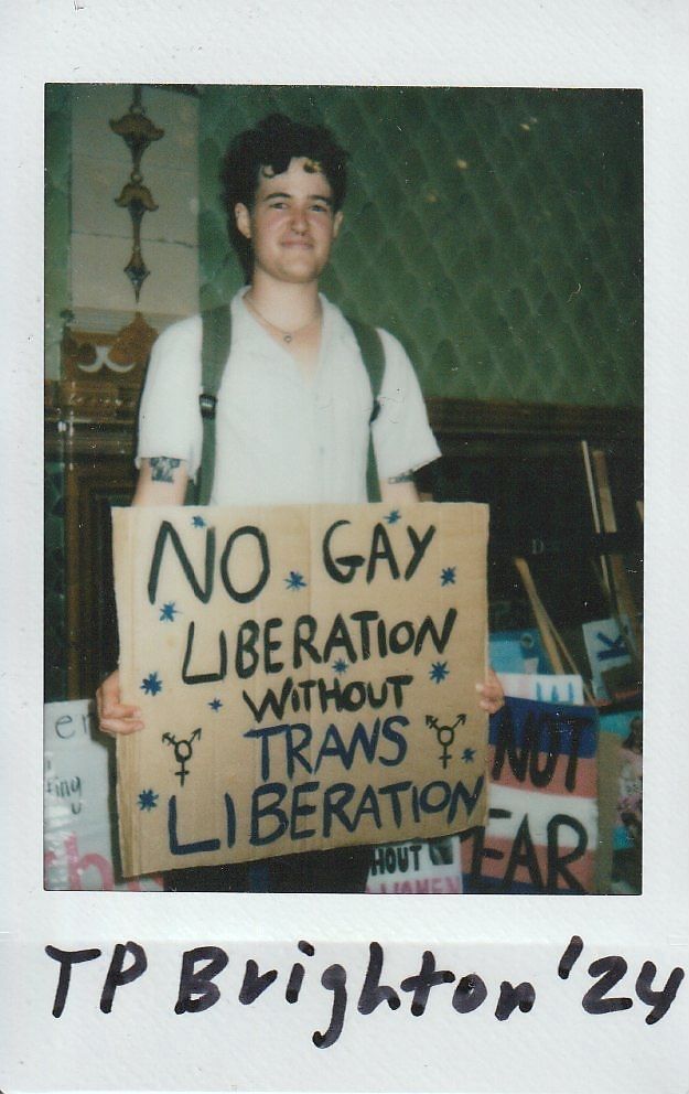 A person holds a sign saying “No gay liberation without trans liberation” at an event.
