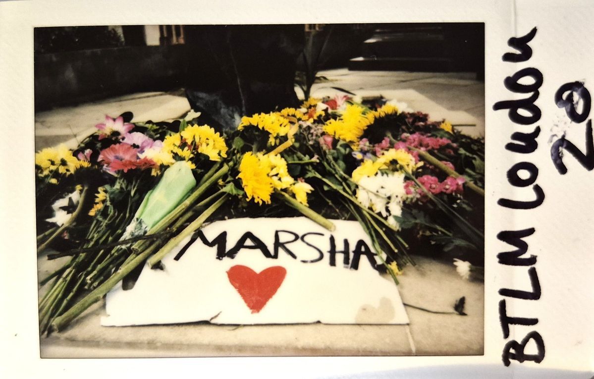 A collection of colorful flowers surrounds a sign reading "MARSHA" with a red heart.