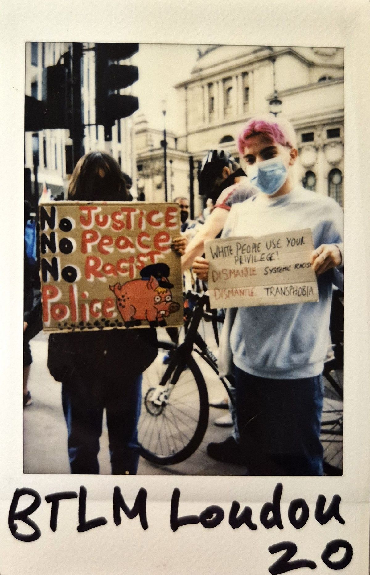 Two people hold protest signs at a protest.