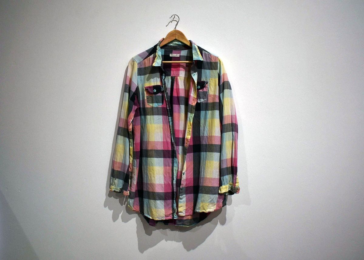 A colorful plaid shirt is displayed on a wooden hanger against a plain white wall.
