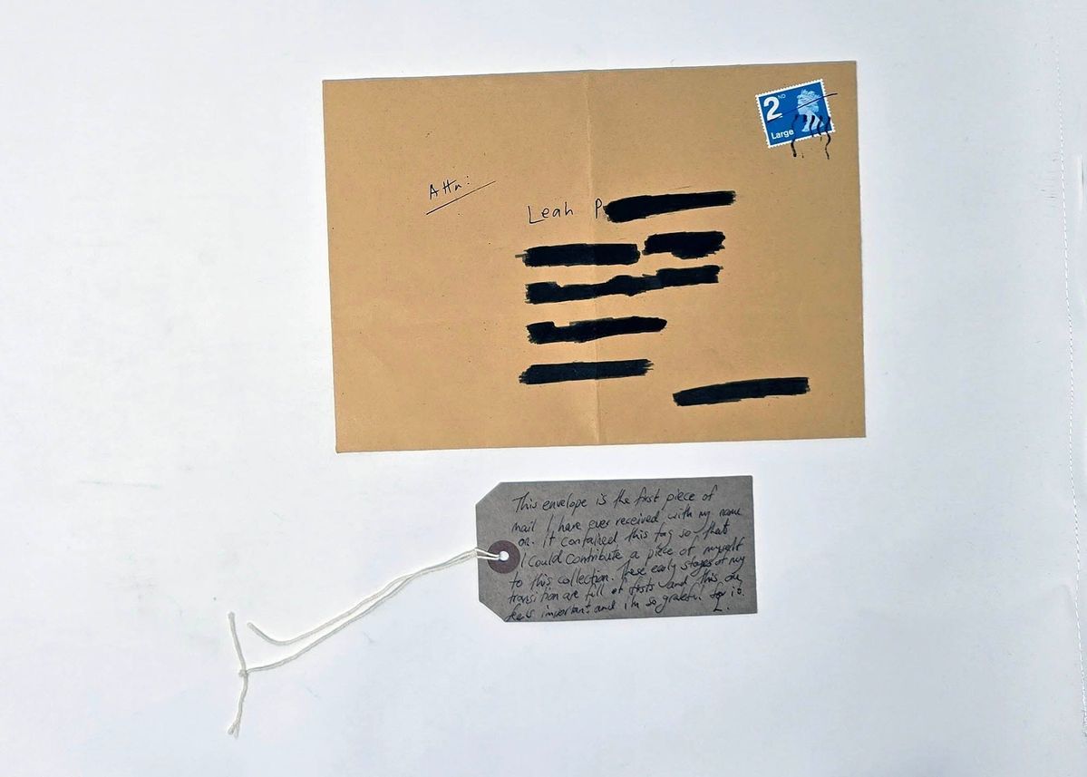 The image shows an envelope with details redacted in black and a handwritten note attached below.