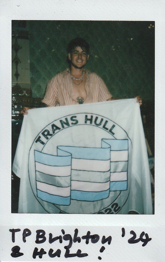 A person smiles while holding a banner that reads "Trans Hull," with handwritten text below.