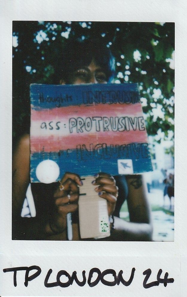 A person is holding a colorful sign with handwritten text, partially concealing their face.