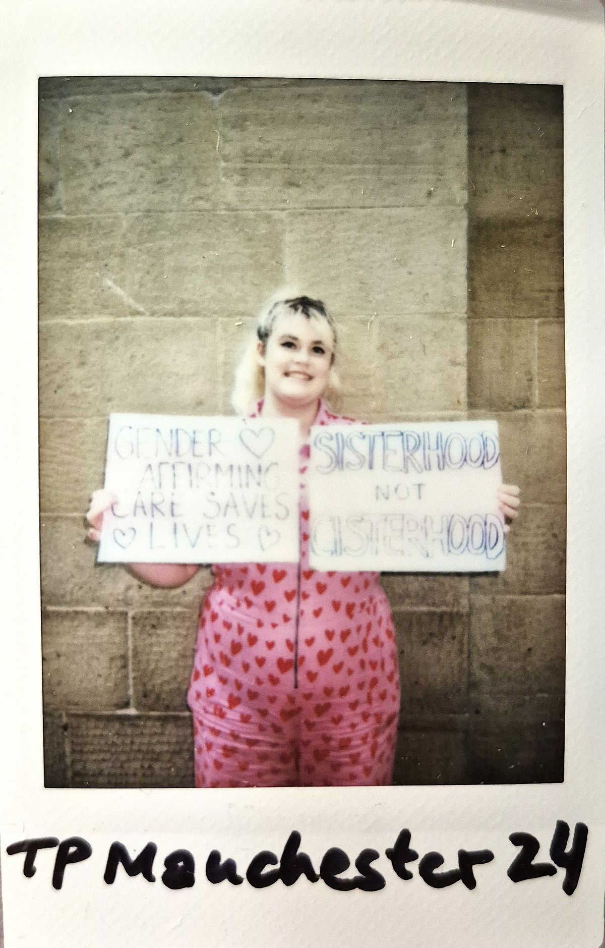 A person in heart-patterned clothing holds two placards.
