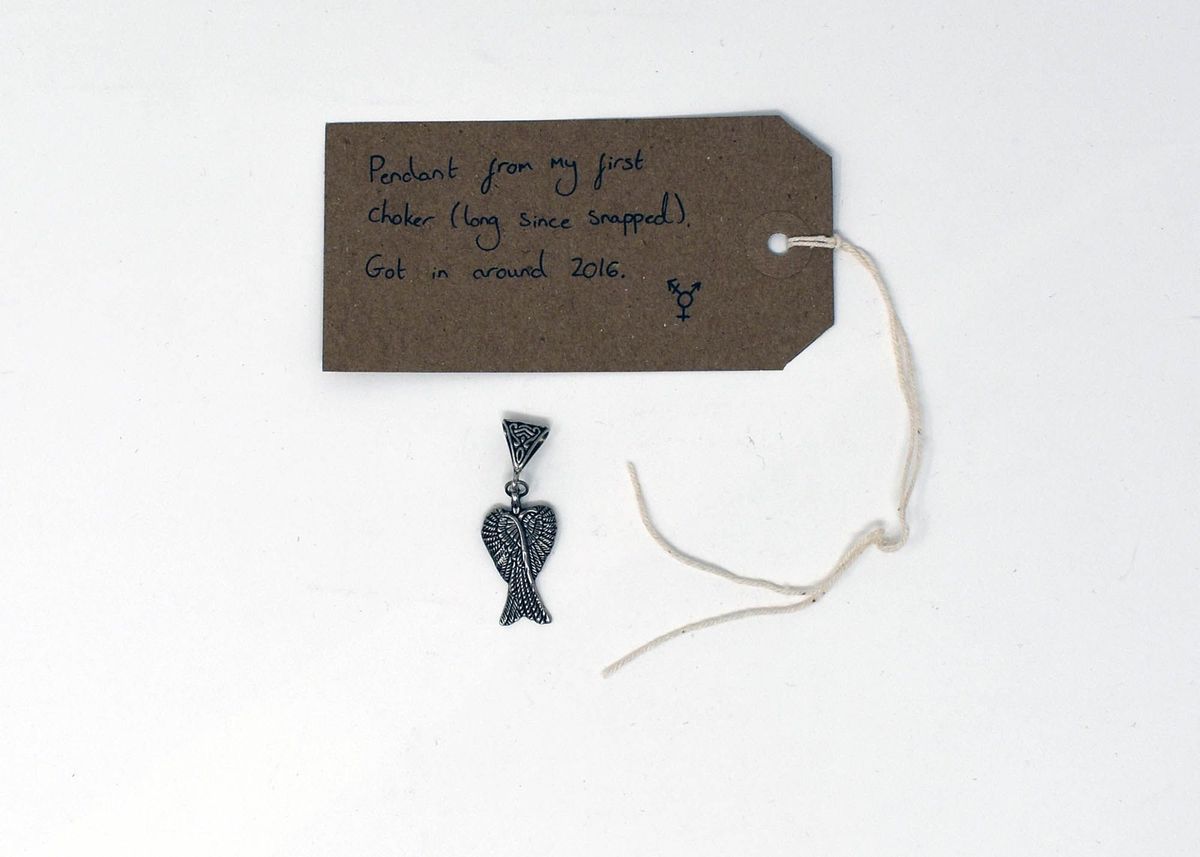 A silver pendant which is next to a brown tag with writing on it.