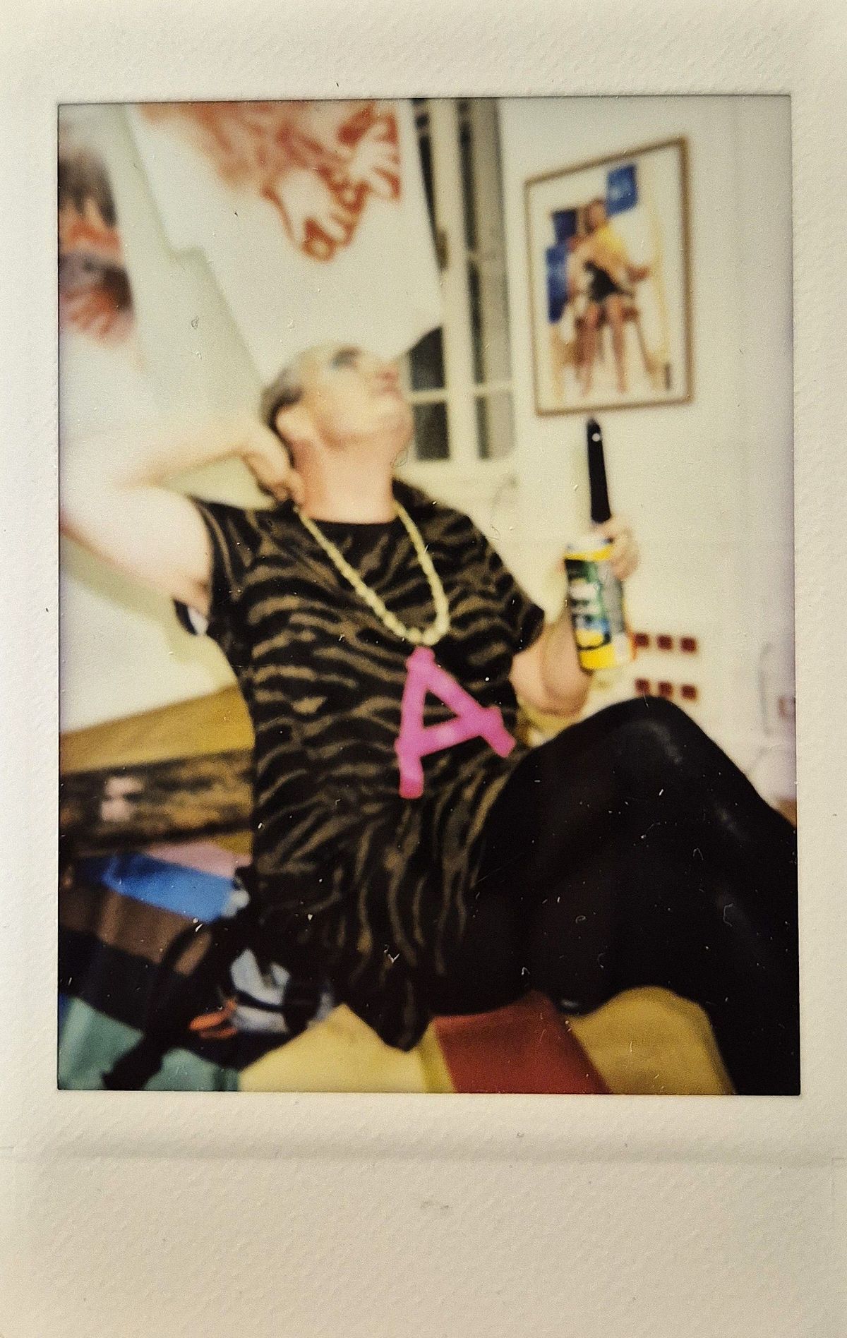 A person is sitting casually, wearing a leopard print top, large necklace with "A".