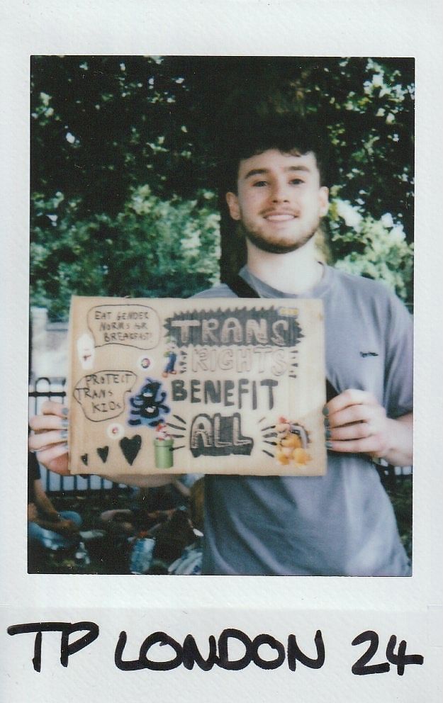 A person is holding a handmade sign advocating for transgender rights at an outdoor event in London.