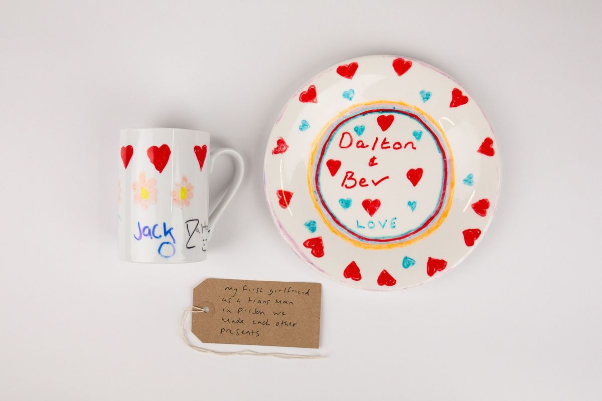 A home made mug and plate made in prison in white ceramic decorated with red and blue hearts. The plate has the text "Dalton & Bev Love". The  mug has the text "Jack" and "Dalton". With a brown, handwritten luggage tag.
