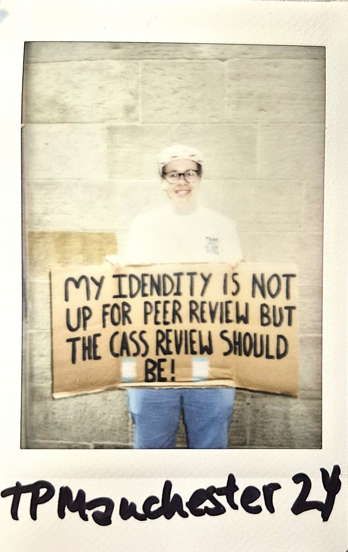 A person holds a cardboard sign with a message about identity smiling in front of a stone