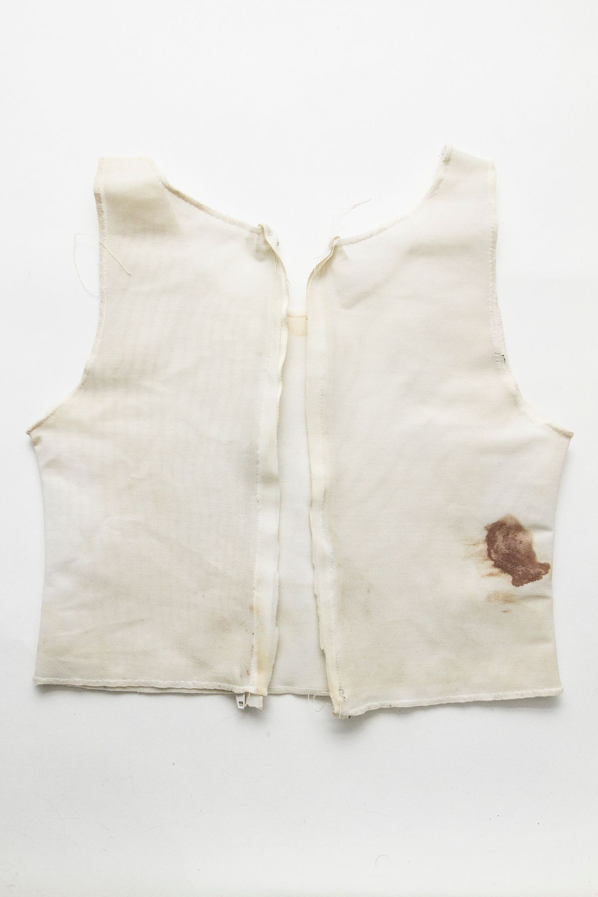 A plain white vest-style binder with a prominent brown stain is laid out flat on a white background.