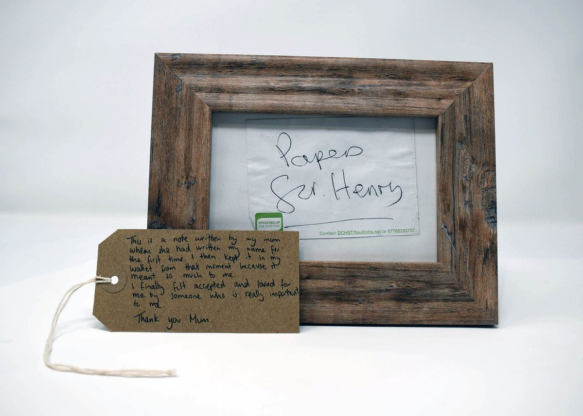A wooden frame displays a handwritten note, accompanied by a heartfelt message on a tag.