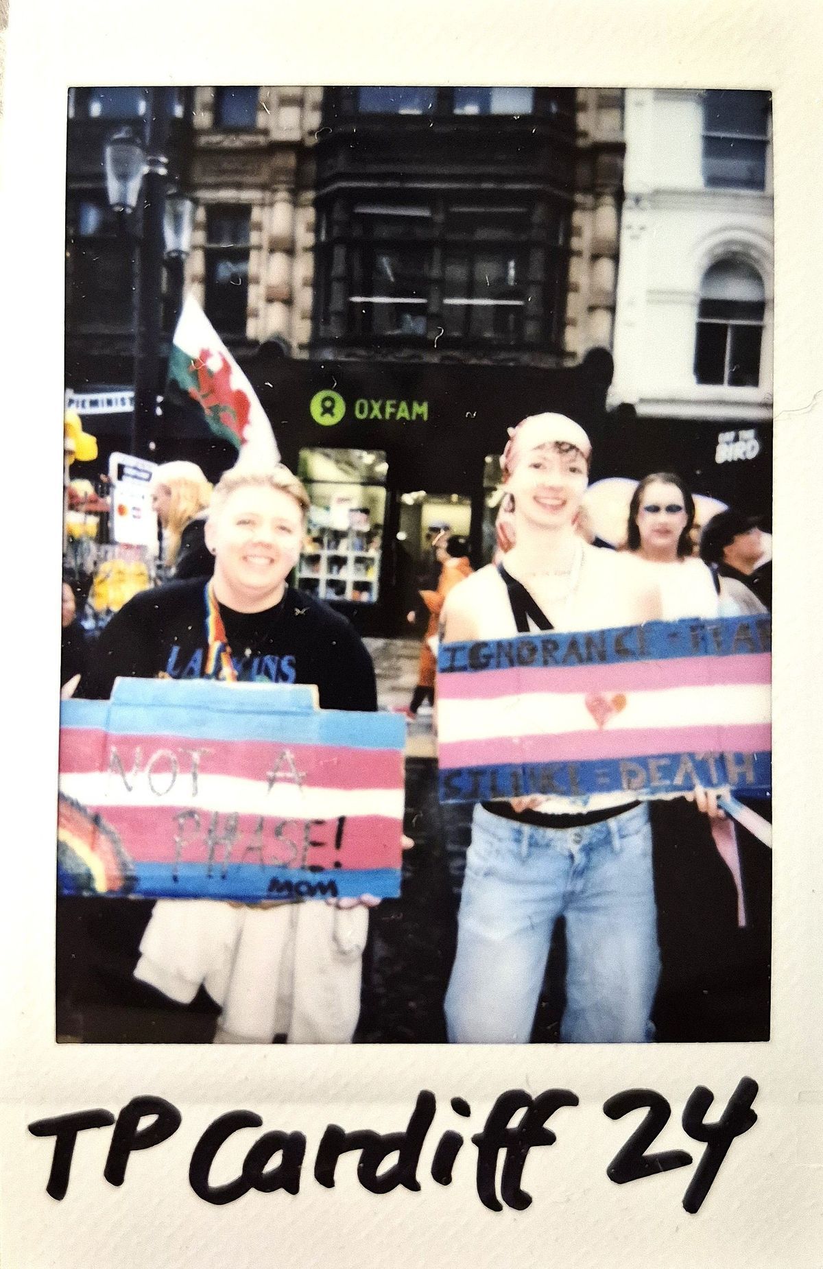 Two people stand together holding colorful protest signs in a lively urban street setting.