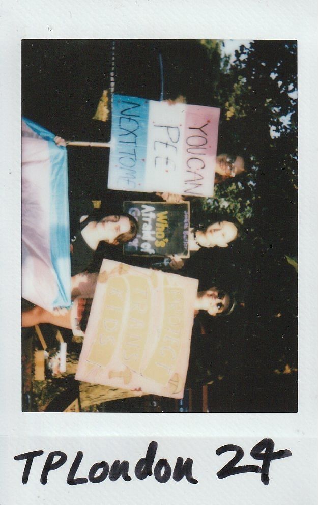 Three people hold signs advocating for transgender rights, standing outdoors with supportive messages.