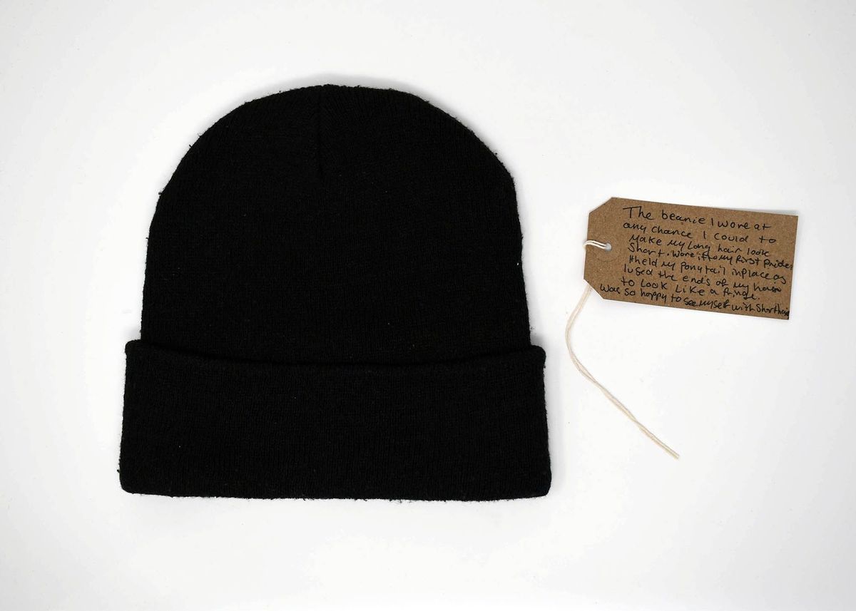 A black beanie is placed beside a handwritten tag with attached string.
