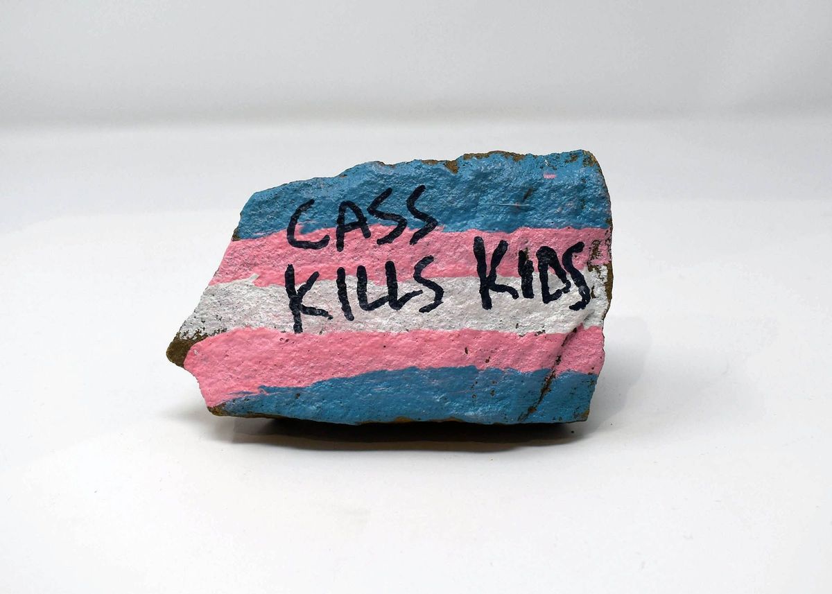 A painted stone displays the words "CASS KILLS KIDS" with colorful stripes.