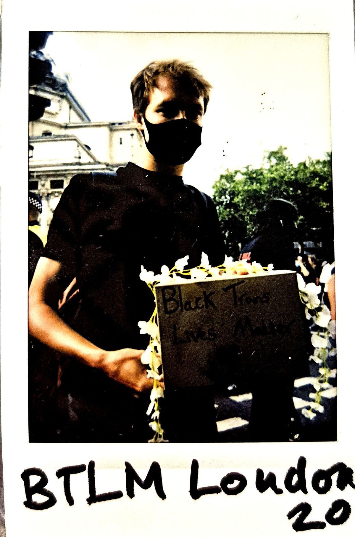 A person wearing a mask holds a sign advocating for Black Trans Lives Matter at a London protest.